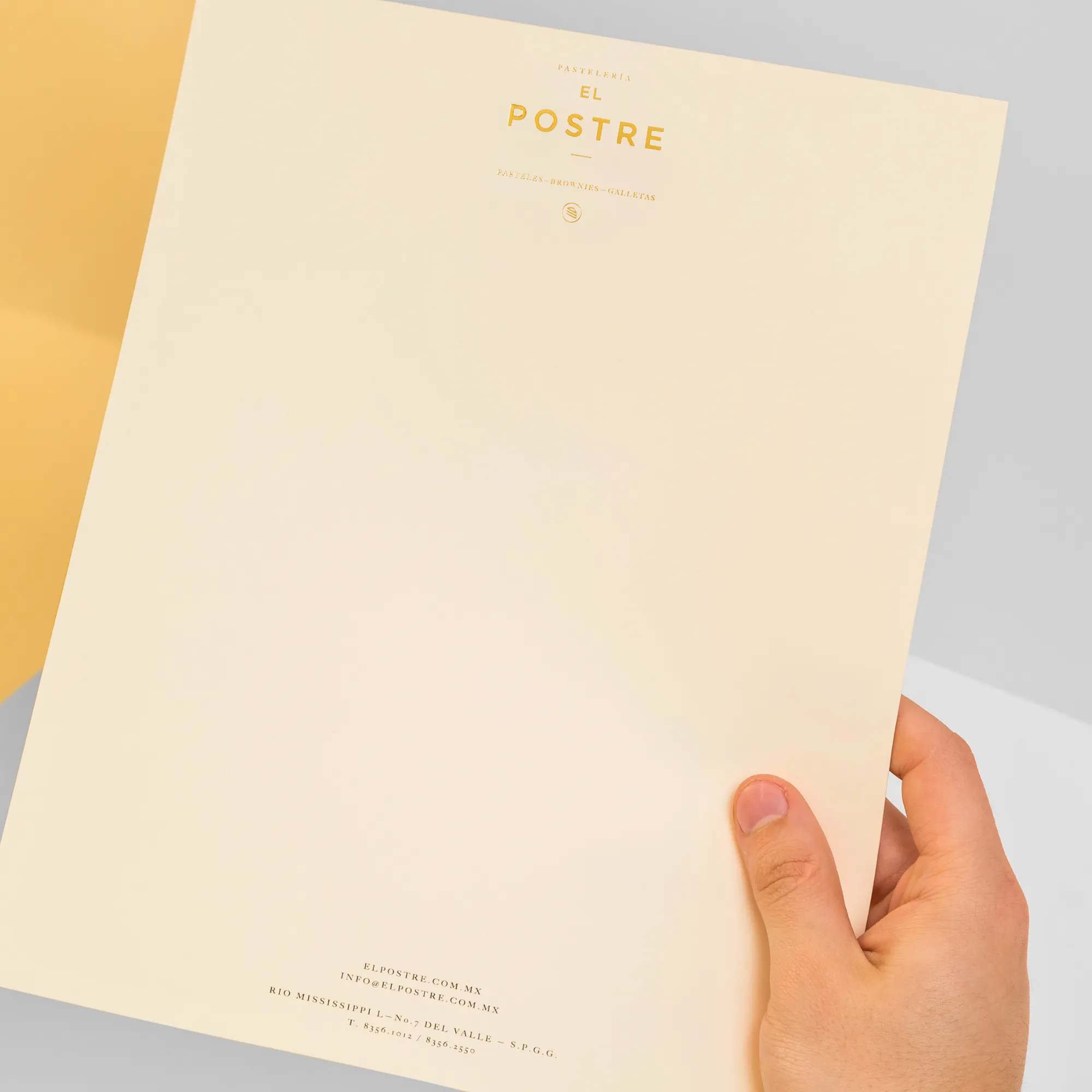 Cream-colored letterhead held in hand featuring the name "EL POSTRE" in gold lettering.