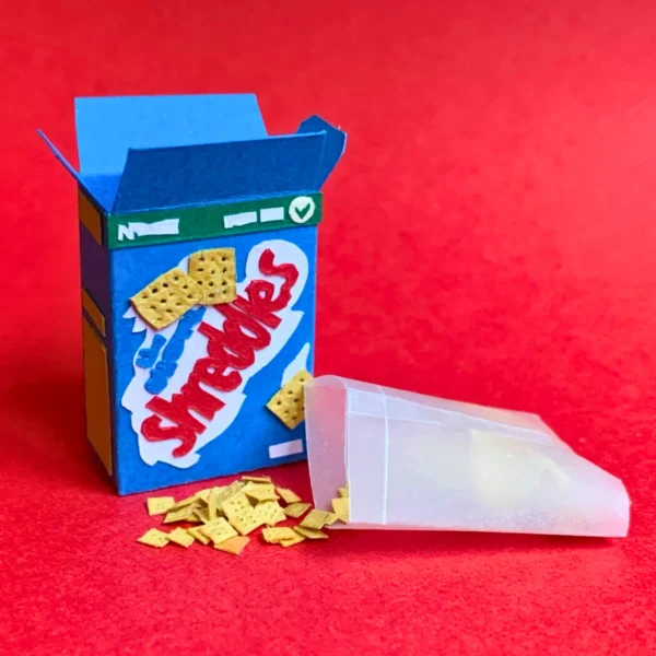 Creative miniature cereal box with shredded pieces spilling out.